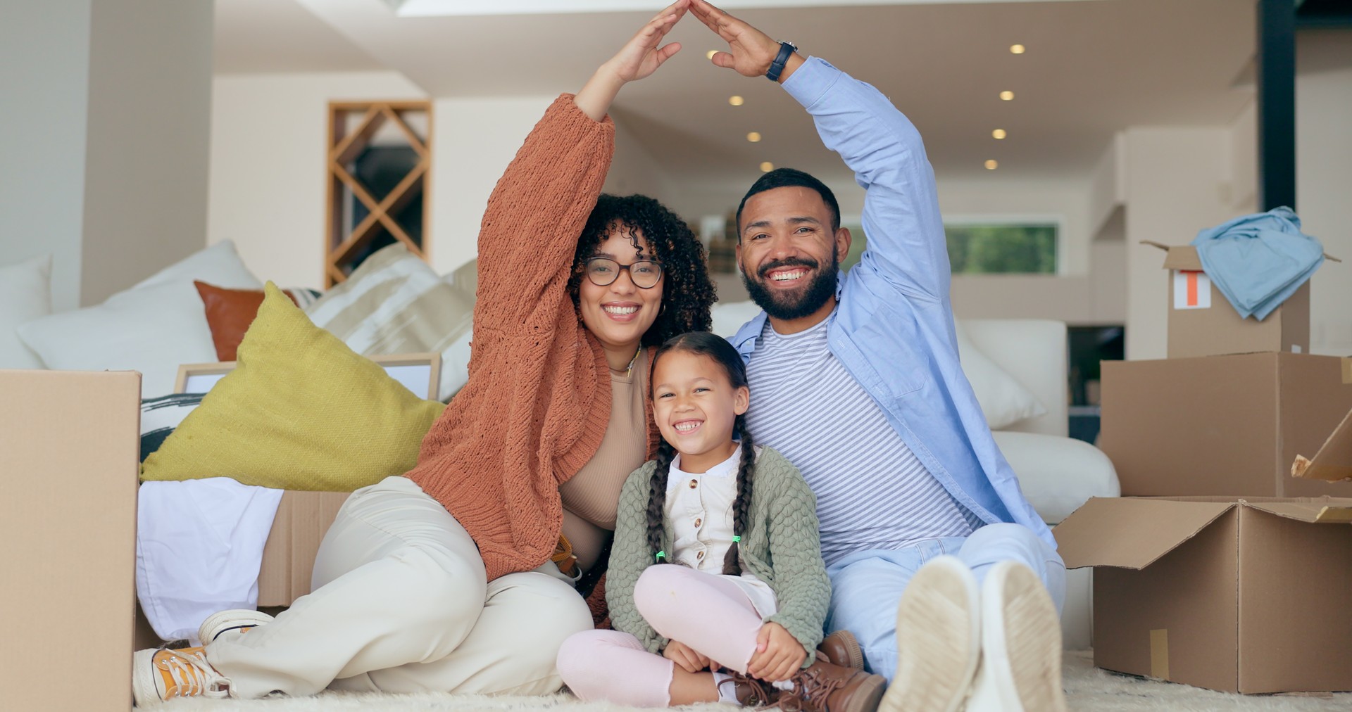 Portrait of happy family with boxes, roof in new home and property insurance, future opportunity and security. Mother, father and child together in living room, real estate and cover in apartment.