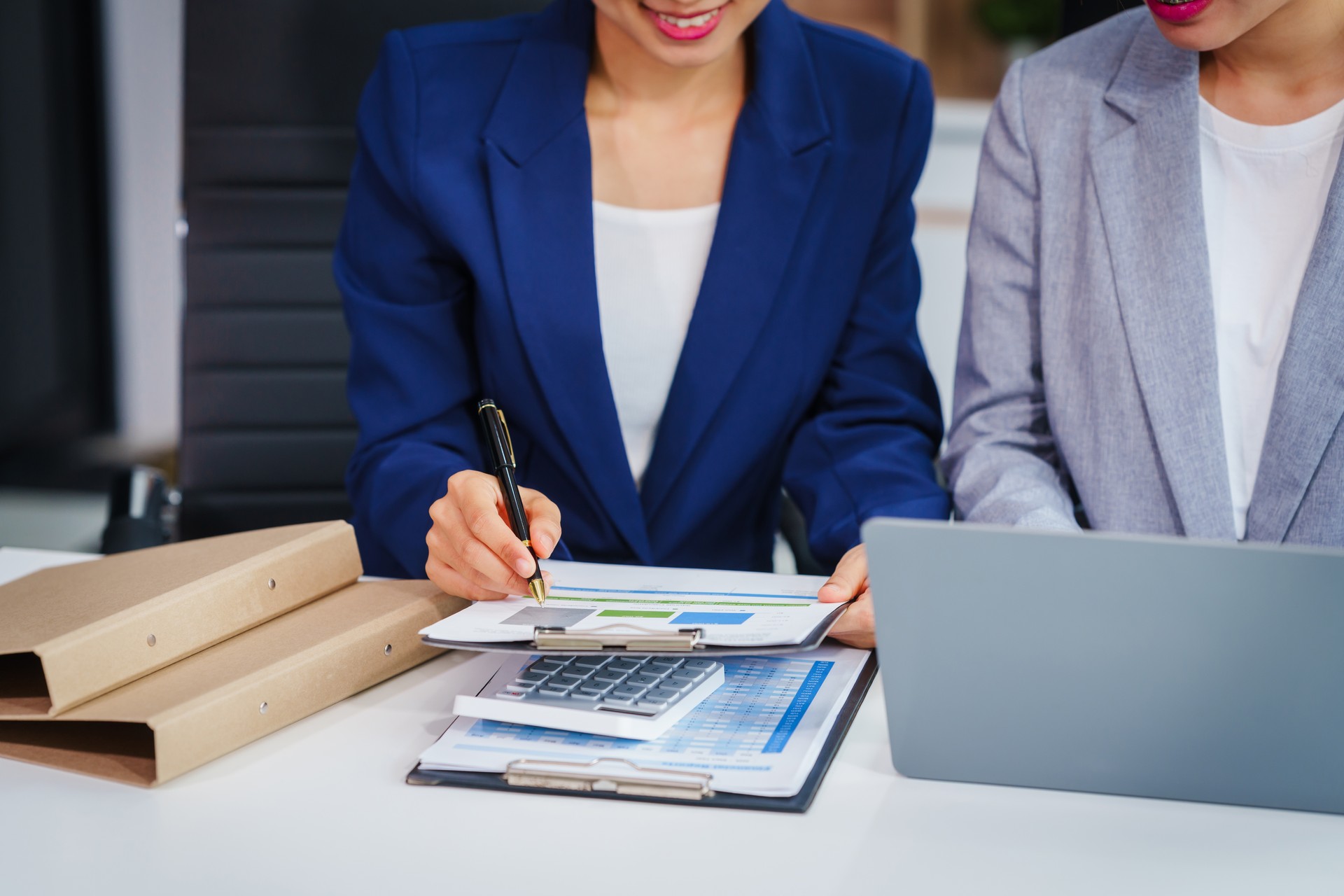 Two Asian businesswomen collaborate on stock market strategies and financial services, exchanging comments and suggestions on loan applications and investment opportunities.